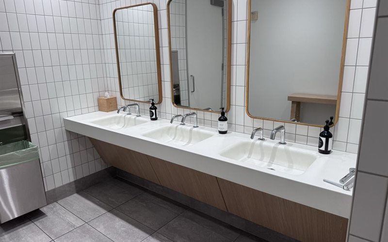 Commercial restroom sink counter with three faucets and mirrors in a Sacramento facility