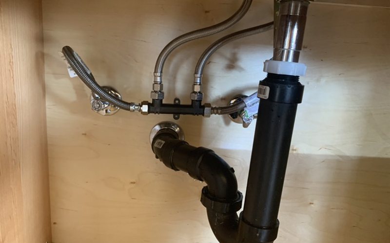 Commercial kitchen sink supply stops, mixing valve and P-trap installed under a Sacramento sink