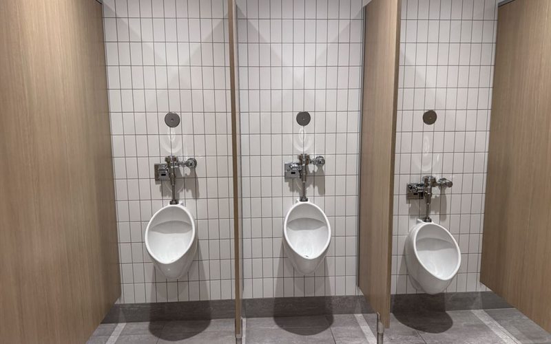 Row of wall-mounted commercial urinals with flush valves in a Sacramento building restroom